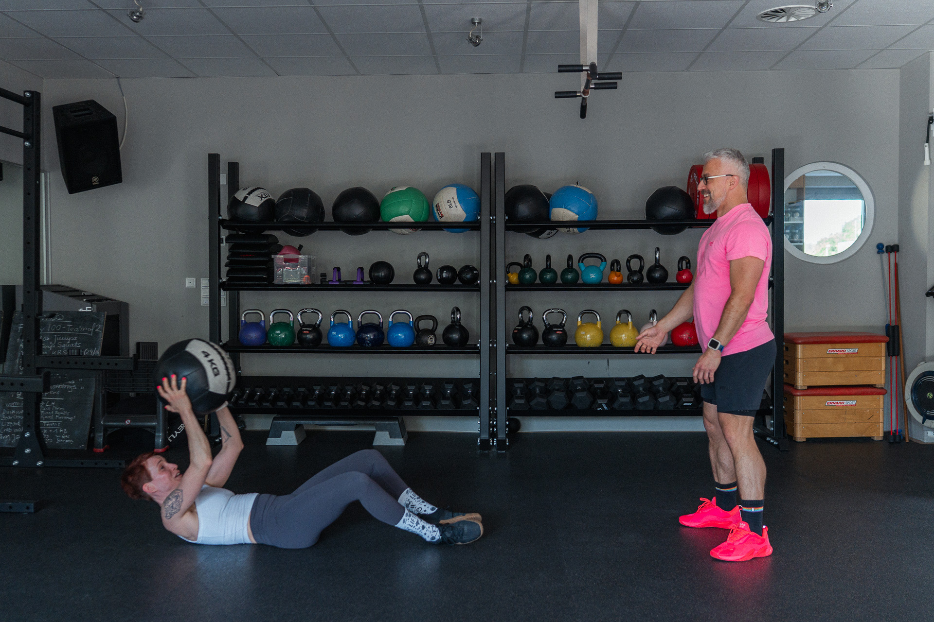 Thomas Kuballa coacht lächelnd eine Klientin bei Sit-ups mit Medizinball